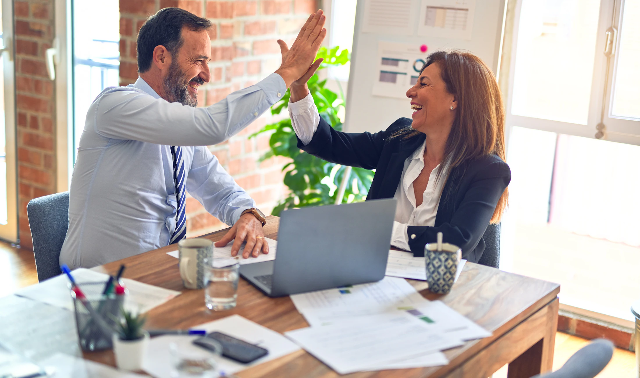 Two colleagues celebrating with a high five at a meeting table
